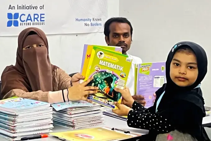 A CBB volunteer hands school books to a student
