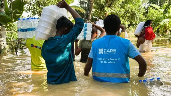 Men carry CBB food sacks through floodwater