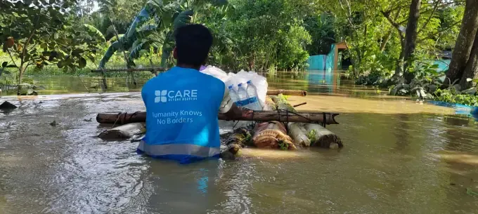 A CBB volunteer carries a relief pack through floodwater
