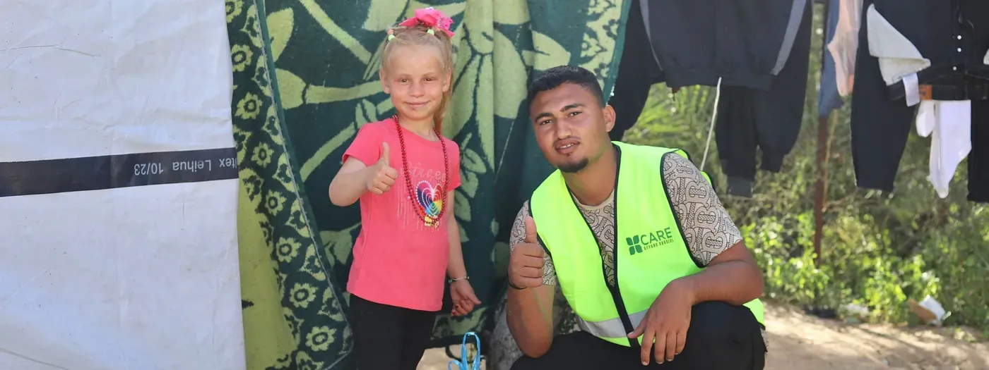 A CBB volunteer and a smiling young girl give a thumbs up together at a camp